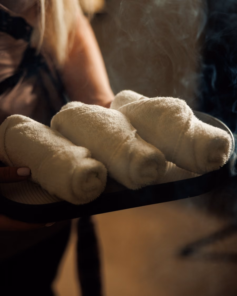 Therapist carrying a tray of hot rolled towels in steam, part of the Royal Hammam ritual at Lavana Spa
