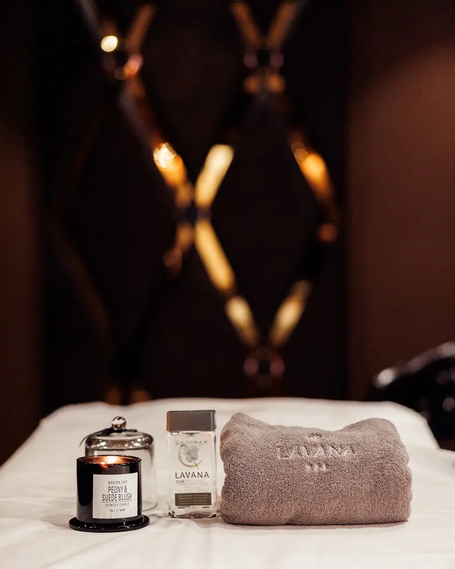 A scented candle, hand wash and folded towel on a treatment bed at Lavana Spa Al Barsha