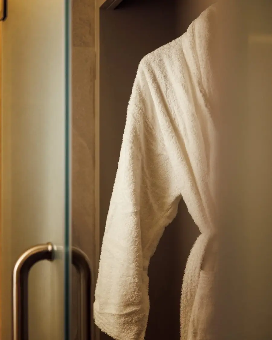 A white bathrobe hanging beside the shower door at Lavana Spa DIFC
